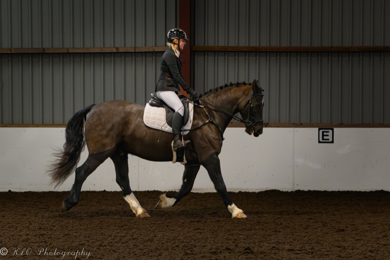 A woman riding a horse in an indoor riding arena.