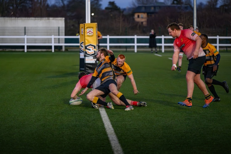 A group of rugby players compete for possession of the ball on a field, with some players on the ground and others standing nearby, during a game.