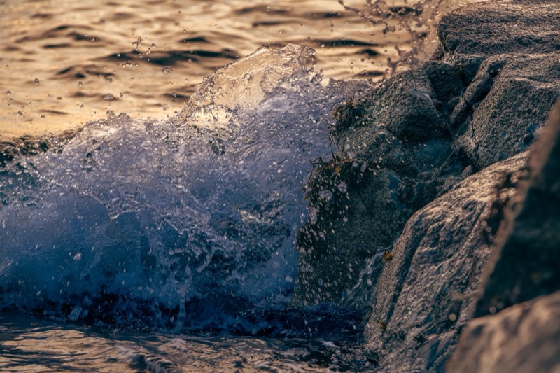 Waves crashing against rocks on a shoreline with a sunset or sunrise reflection on the water